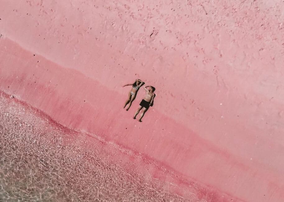 A couple relaxing on the soft pink sands of Pink Beach, Komodo National Park, with crystal-clear waters gently washing ashore