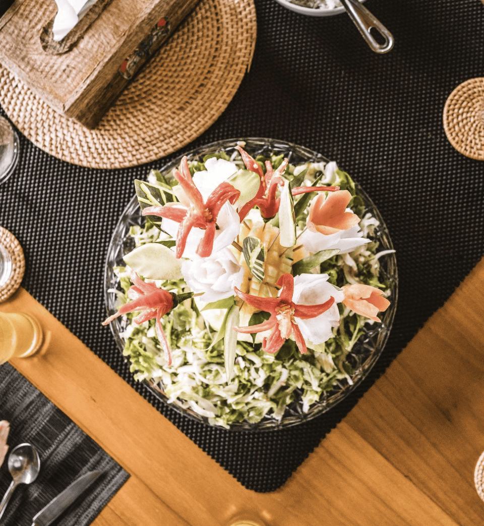 A flat lay image of a colorful salad, on a black placemat and wooden table onboard the yacht Jakare.