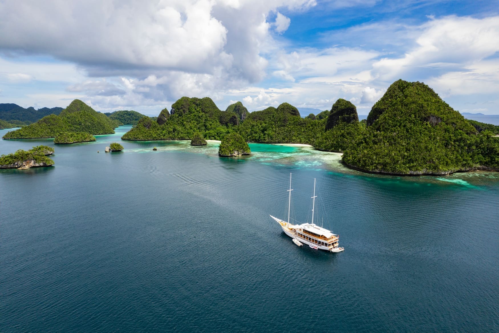 The white yact Fenides anchored in between vibrant green tropical islands and blue waters in Indonesia.