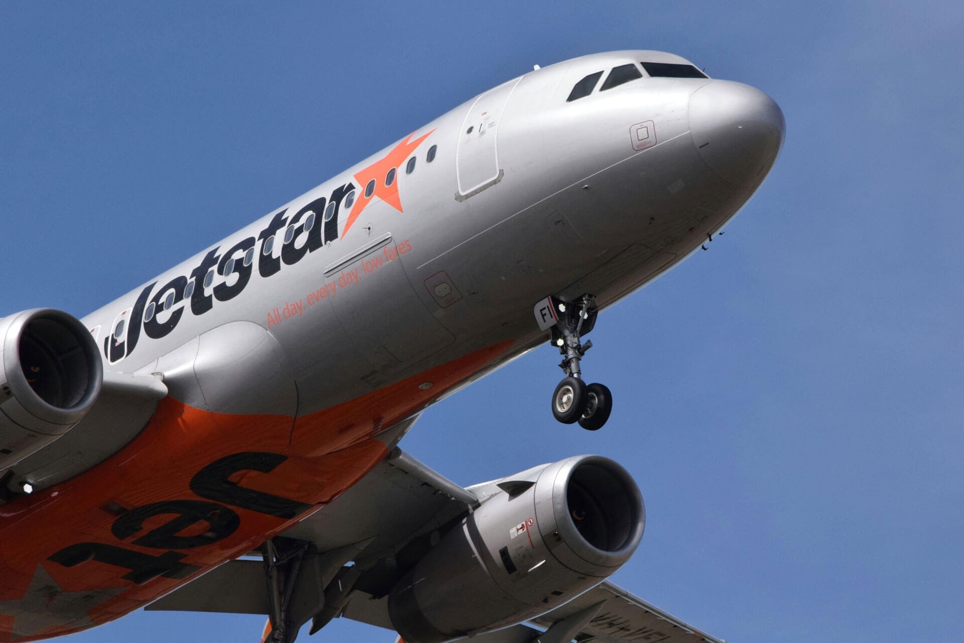 etstar Asia Airbus A320 aircraft approaching landing with landing gear down against a clear blue sky.