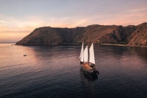 Luxury boat with white sails in the meddle of a bay with mountains on one side.