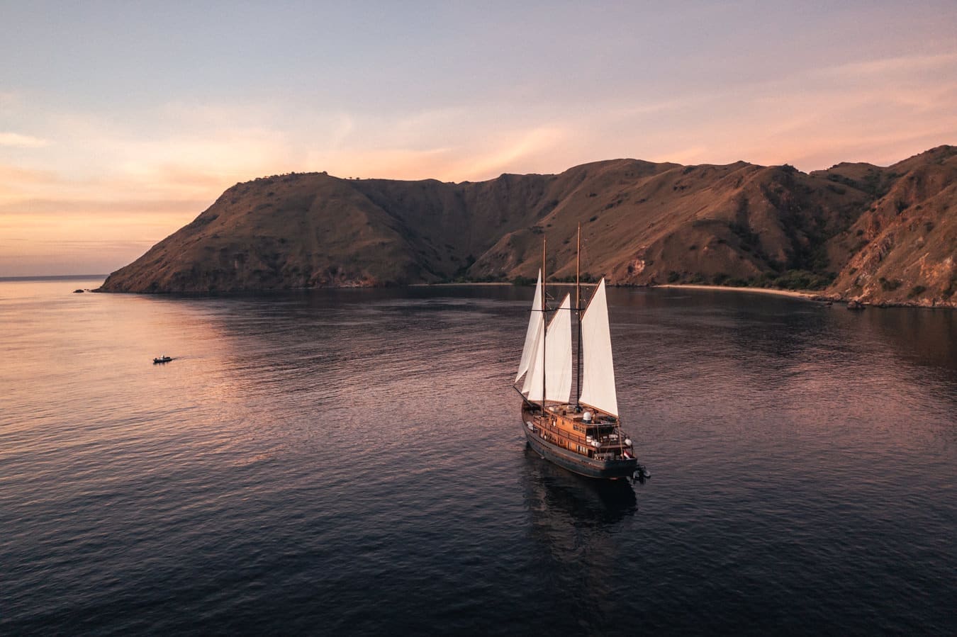Luxury boat with white sails in the meddle of a bay with mountains on one side.