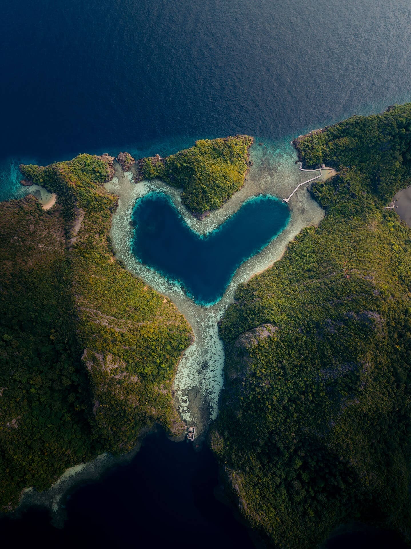 A heart shaped lagoon with blue water surrounded by lush mountains.